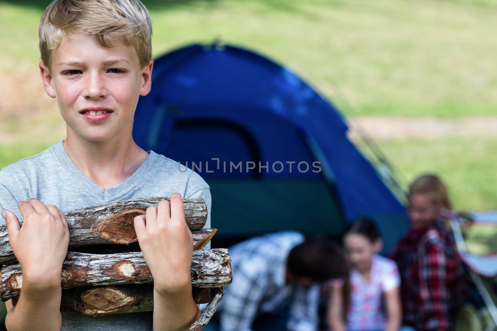 Boy carrying firewood outside the tent and family in background