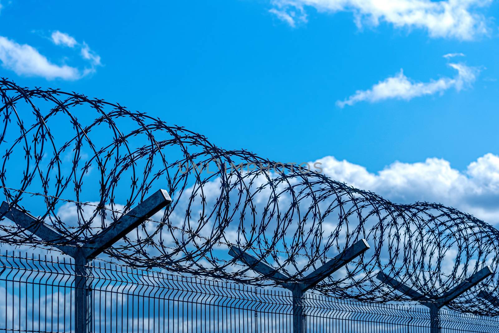 fence with barbed wire against blue sky with clouds, security concept