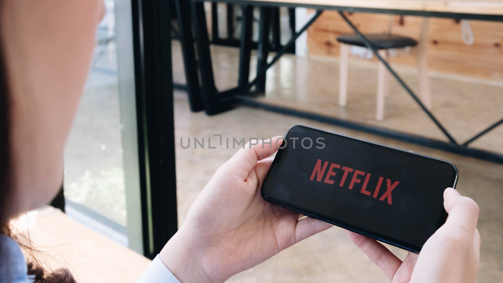 CHIANG MAI, THAILAND, JUN 7 , 2020: Young woman in a hammock opening Netflix in her smartphone. Millennial girl resting with her cell phone in her hands and the Netflix logo in the screen.

