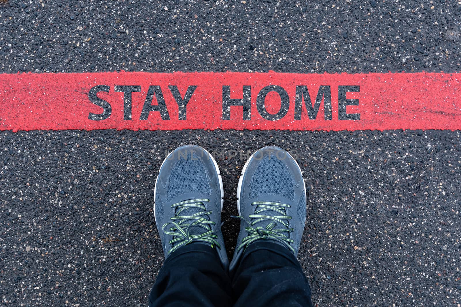 man in sneakers standing next to a red line with text STAY HOME, restriction or safety warning concept