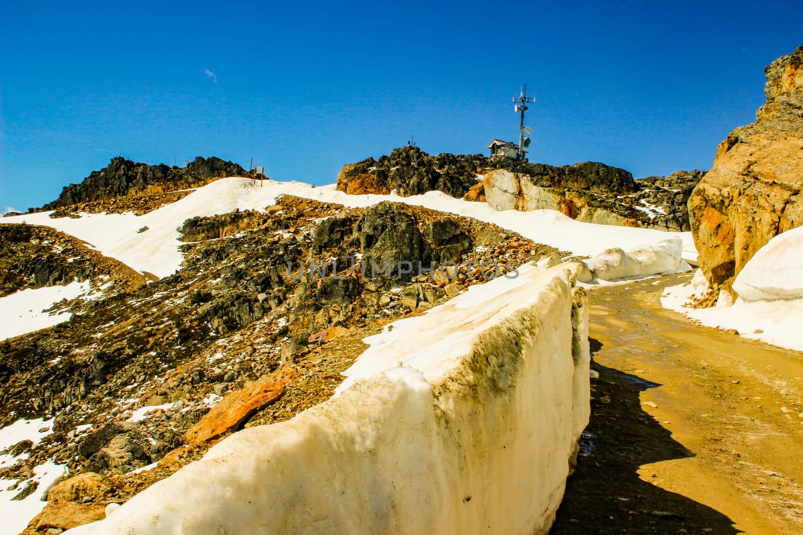 Snow-capped peaks on a background of white clouds and blue sky. Green hills and dense forests on the slopes. Morning sun shines on the rock wall.