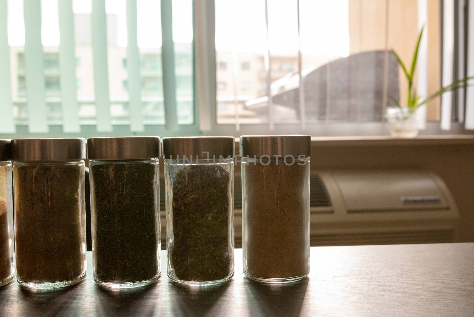 Assortments of spices, white pepper, chili flakes, lemongrass, coriander and cumin seeds in jars on grey stone background