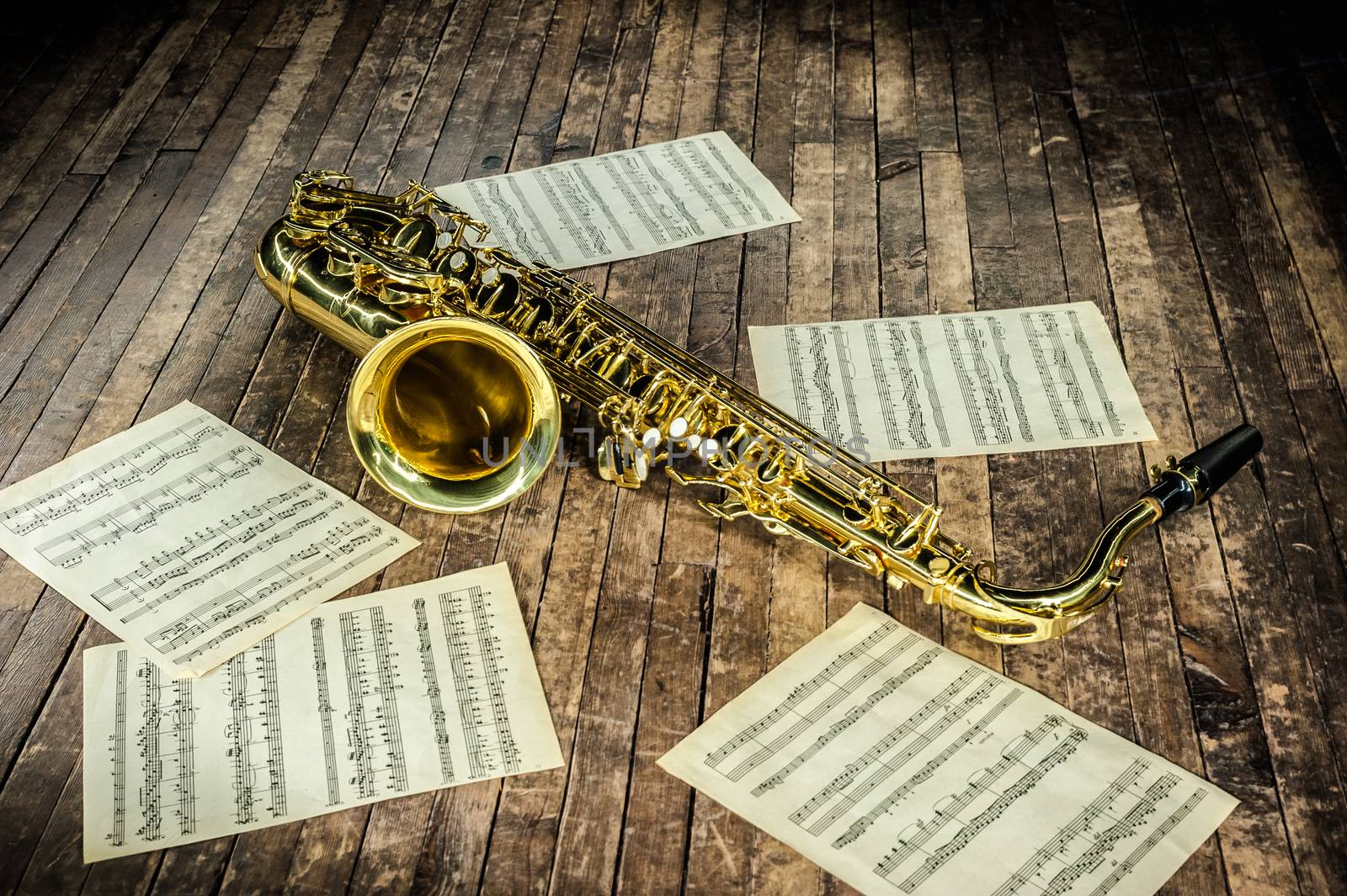 beautiful yellow saxophone and paper with music score notes lying on a vintage wooden stage
