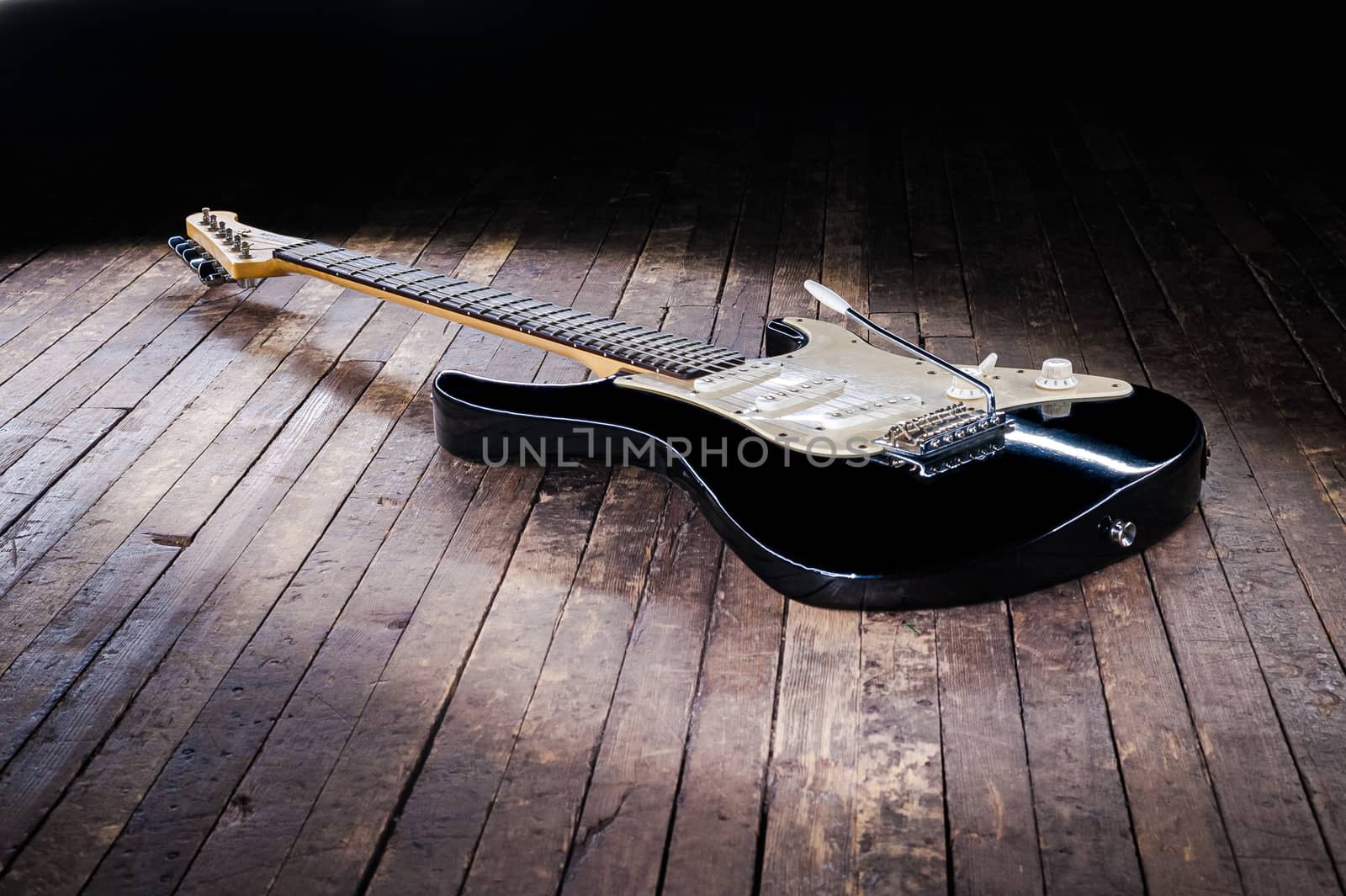 black and white electric guitar with a yellow signature stamp lies on a wooden stage