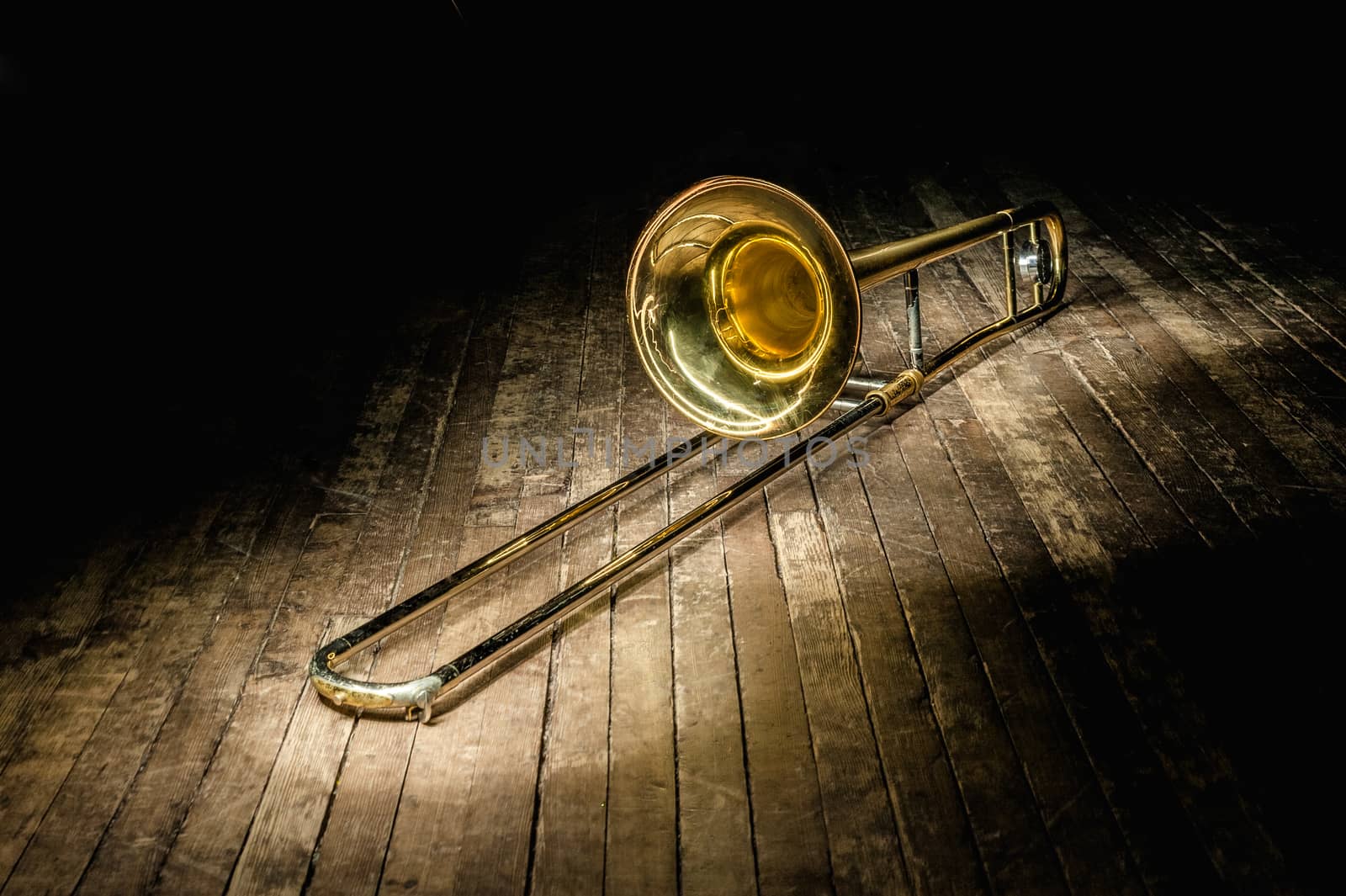 golden brass instrument trombone lies on a dark brown wooden stage in the rays of light