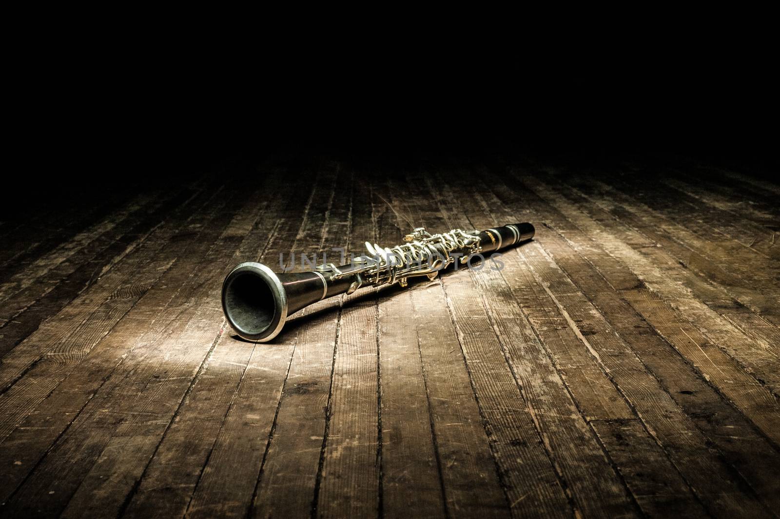 a black woodwind clarinet lies on a dark brown wooden stage in the rays of light