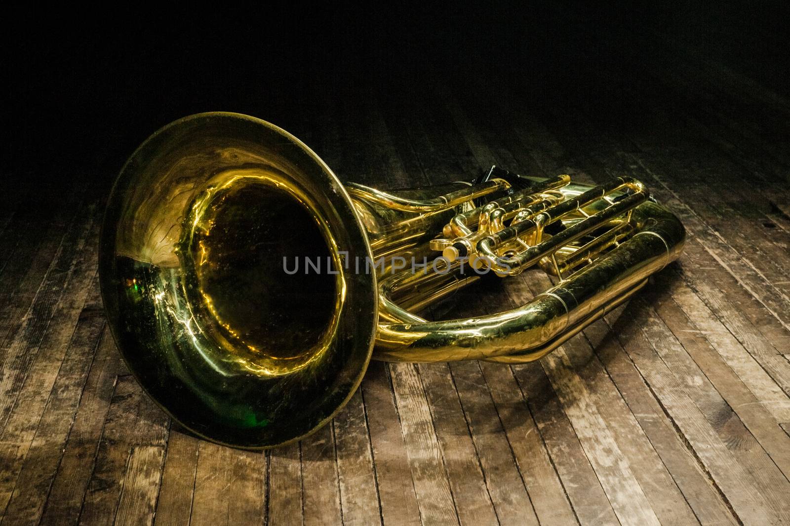 golden brass instrument tuba lies on a brown wooden stage in the light of the spotlight