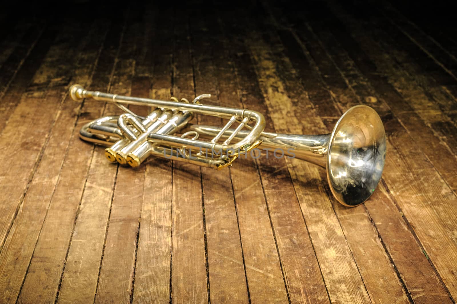 white brass trumpet lies on a wooden stage in the dark