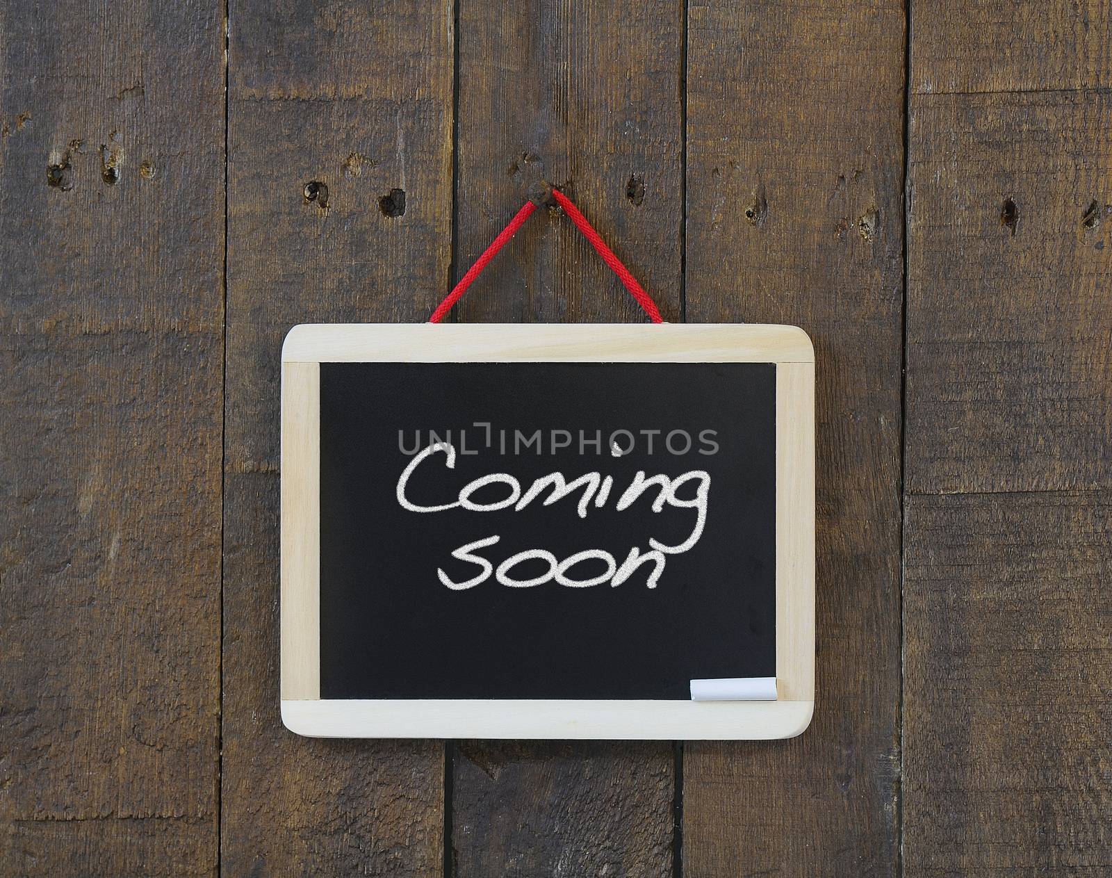 Blackboard hanging on a old wooden wall with phrase Coming soon.