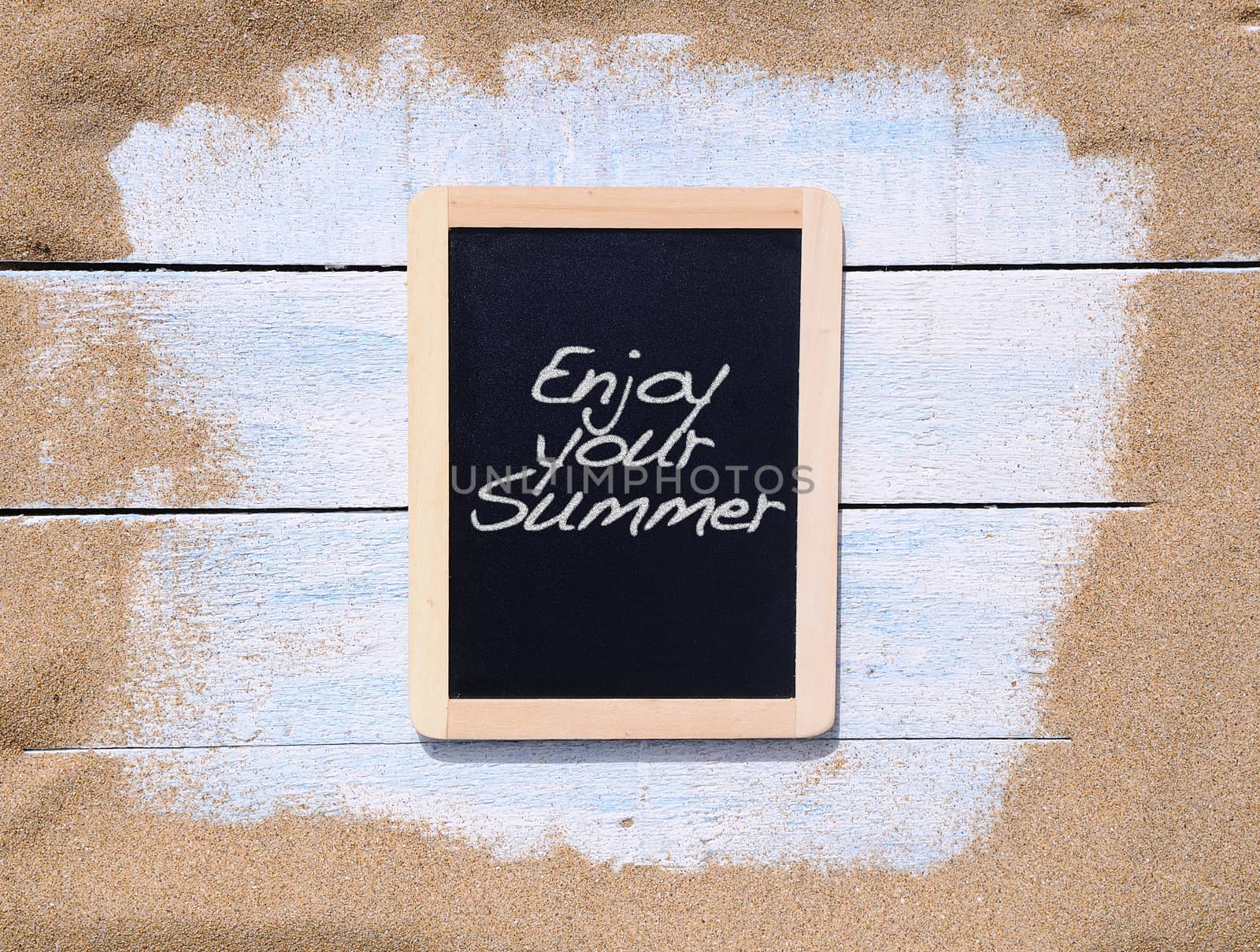 Blackboard on the beach with the phrase Enjoy your summer