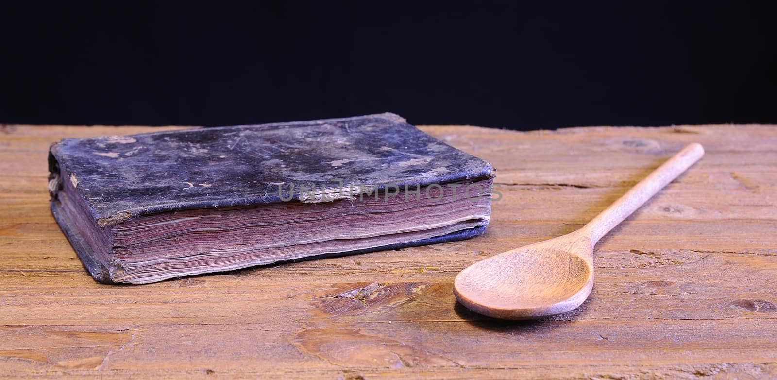 Old cookbook on wooden table with a wooden spoon