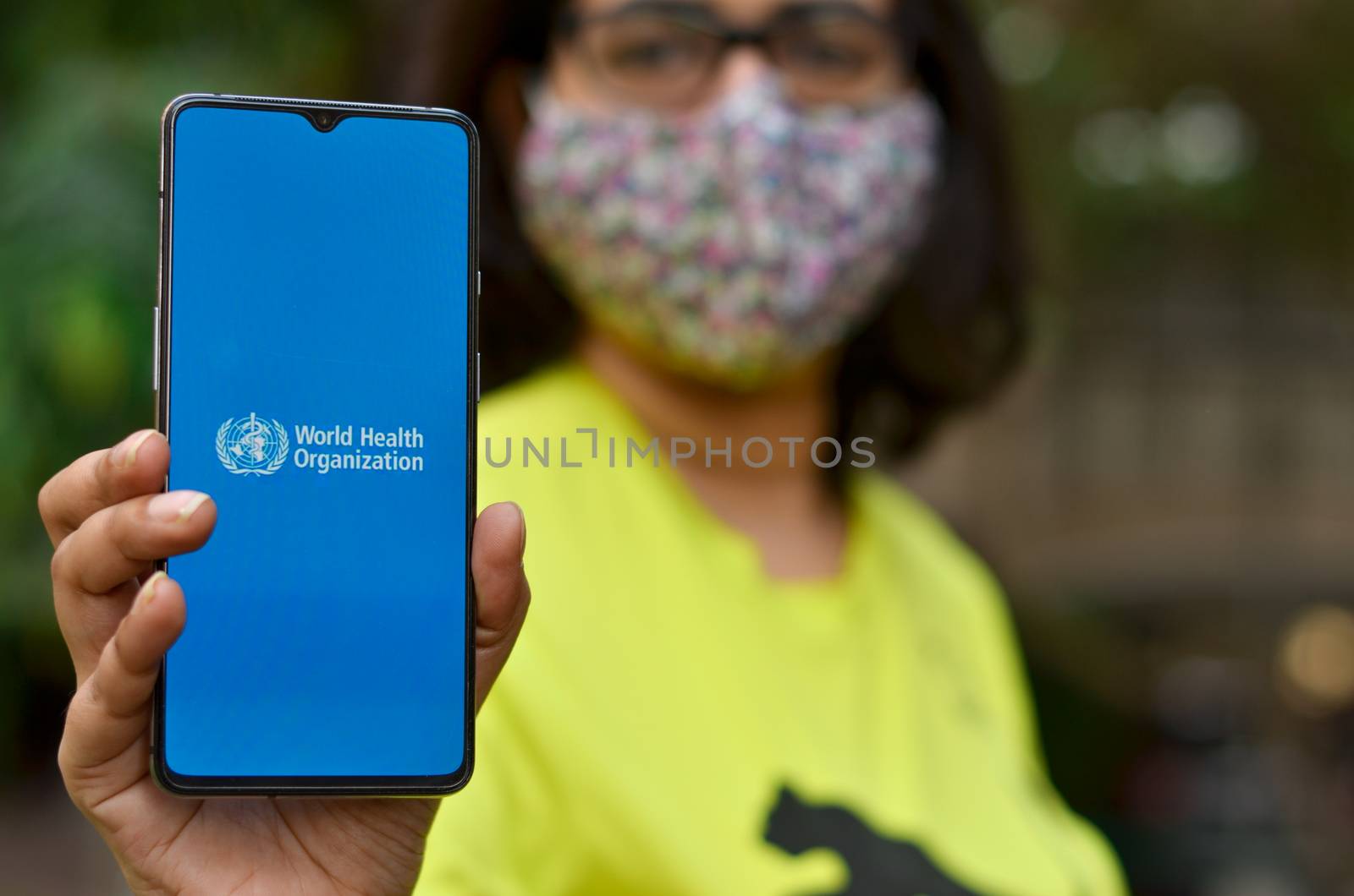USA, 2020. Girl wearing mask showing on her mobile phone screen, World health organization (WHO) landing page & emblem.Specialized agency of United Nations responsible for public health