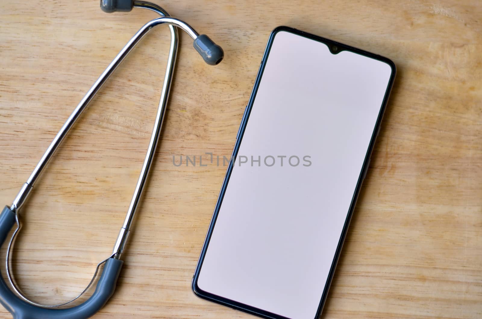 Stethoscope and a mobile phone showing empty white screen kept over a wooden background. Advertising healthcare internet app or health tech software concept