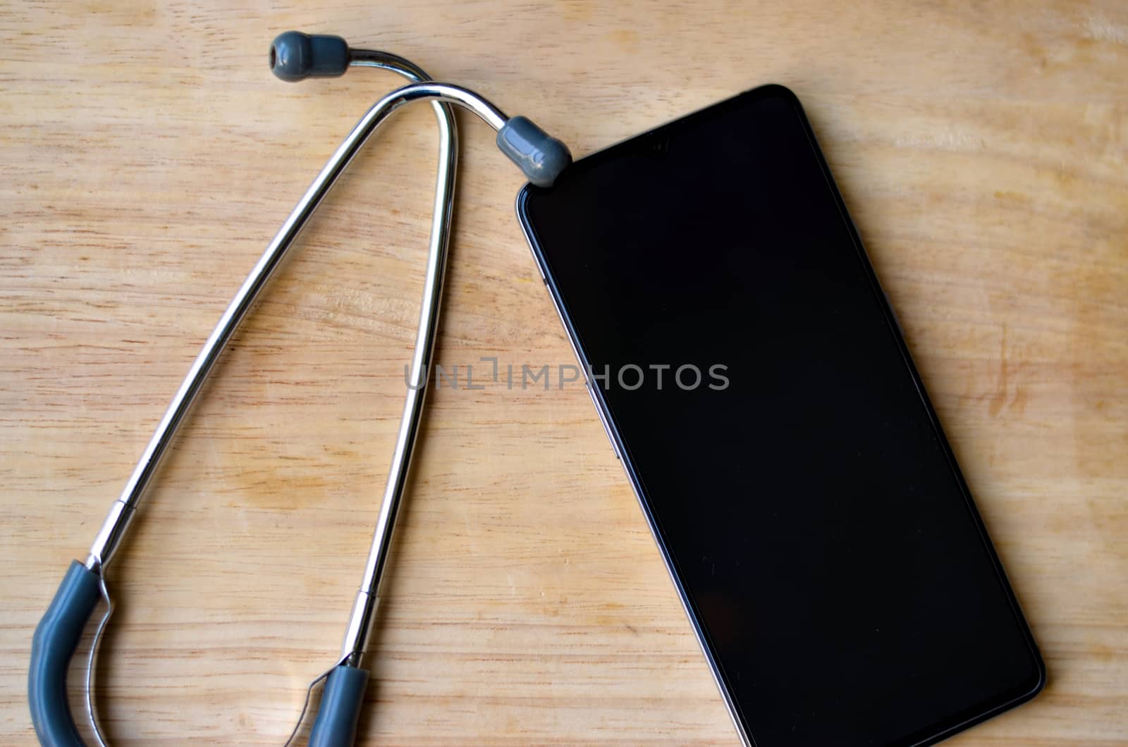 Stethoscope and a mobile phone showing empty black screen kept over a wooden background. Advertising healthcare internet app or health tech software concept