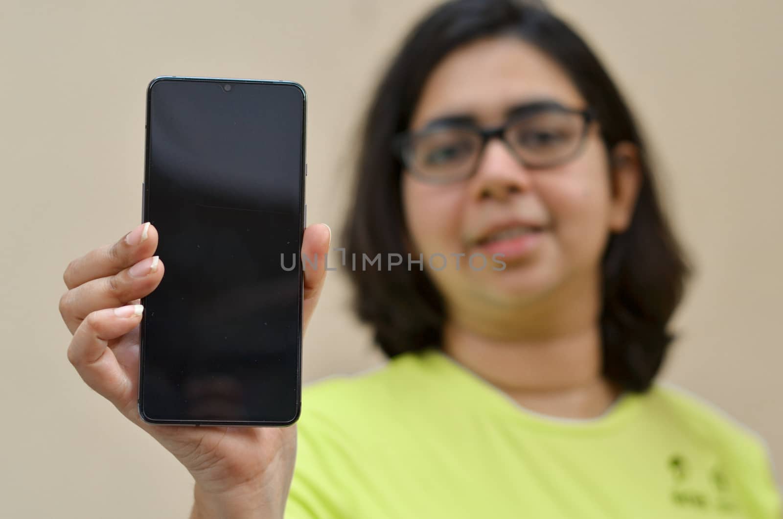 Young Indian woman showing her blank mobile phone black screen against yellow background which can be used for copy space for different apps. Concept Happy smartphone user blank screen for advertising