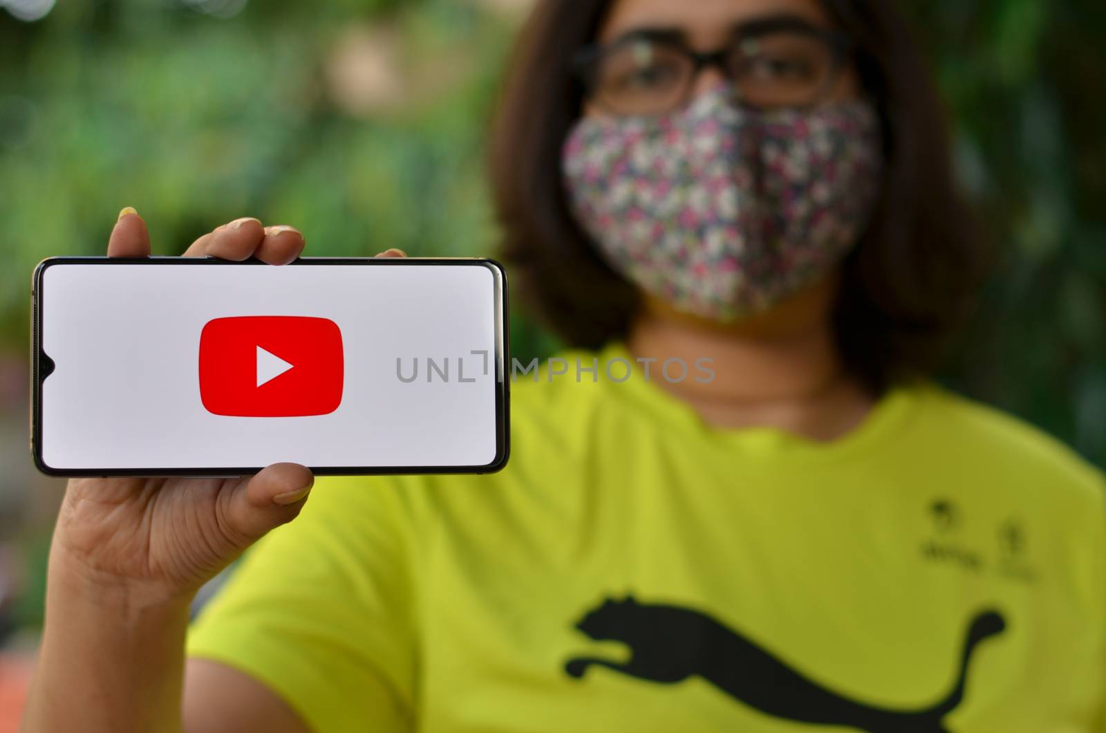 Delhi, India,2020. Girl wearing mask show Youtube app on mobile under home quarantine for Corona virus (Covid-19) disease pandemic. Youtube is very population app among all the generations