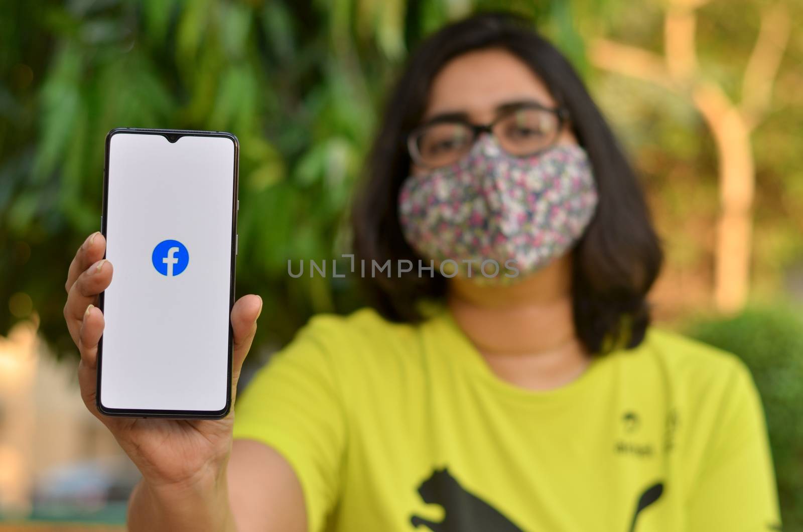 Delhi, India,2020. Girl wearing mask show Facebook app on mobile under home quarantine for Corona virus (Covid-19) disease pandemic. Facebook is very population app among all the generations