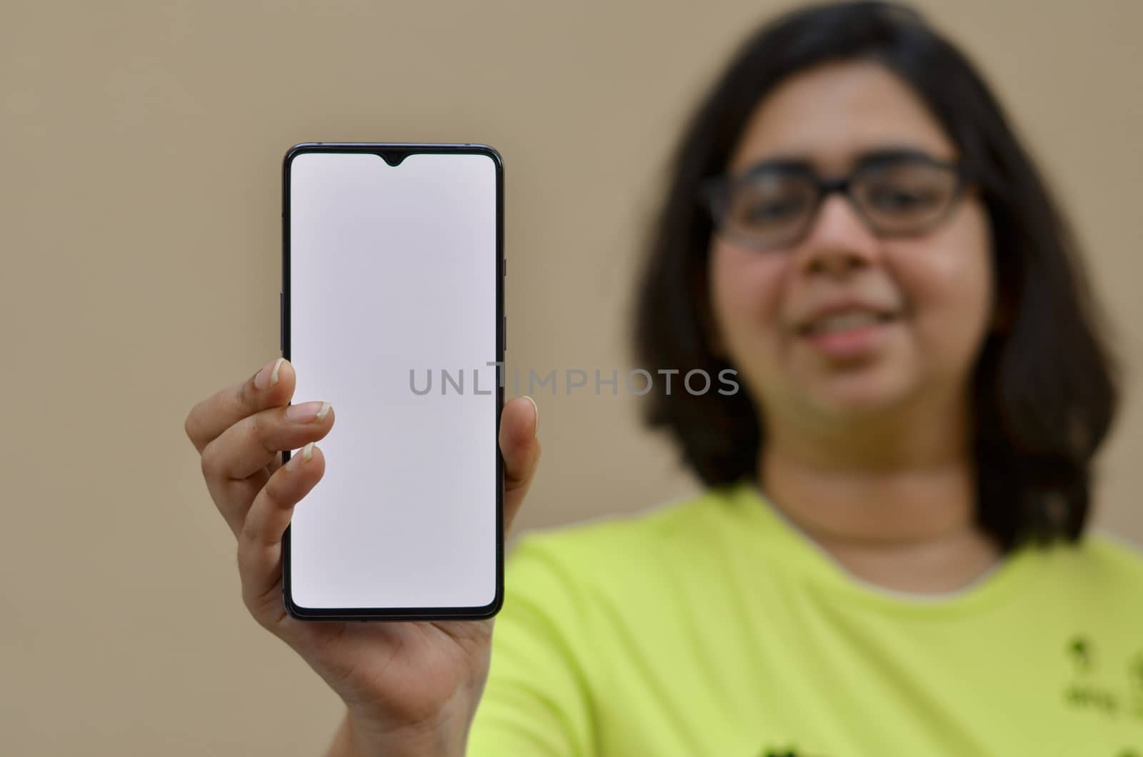 Young woman showing her blank mobile phone white screen against yellow background which can be used for copy space for different apps. Concept Happy smartphone user - blank screen for advertising by jayantbahel