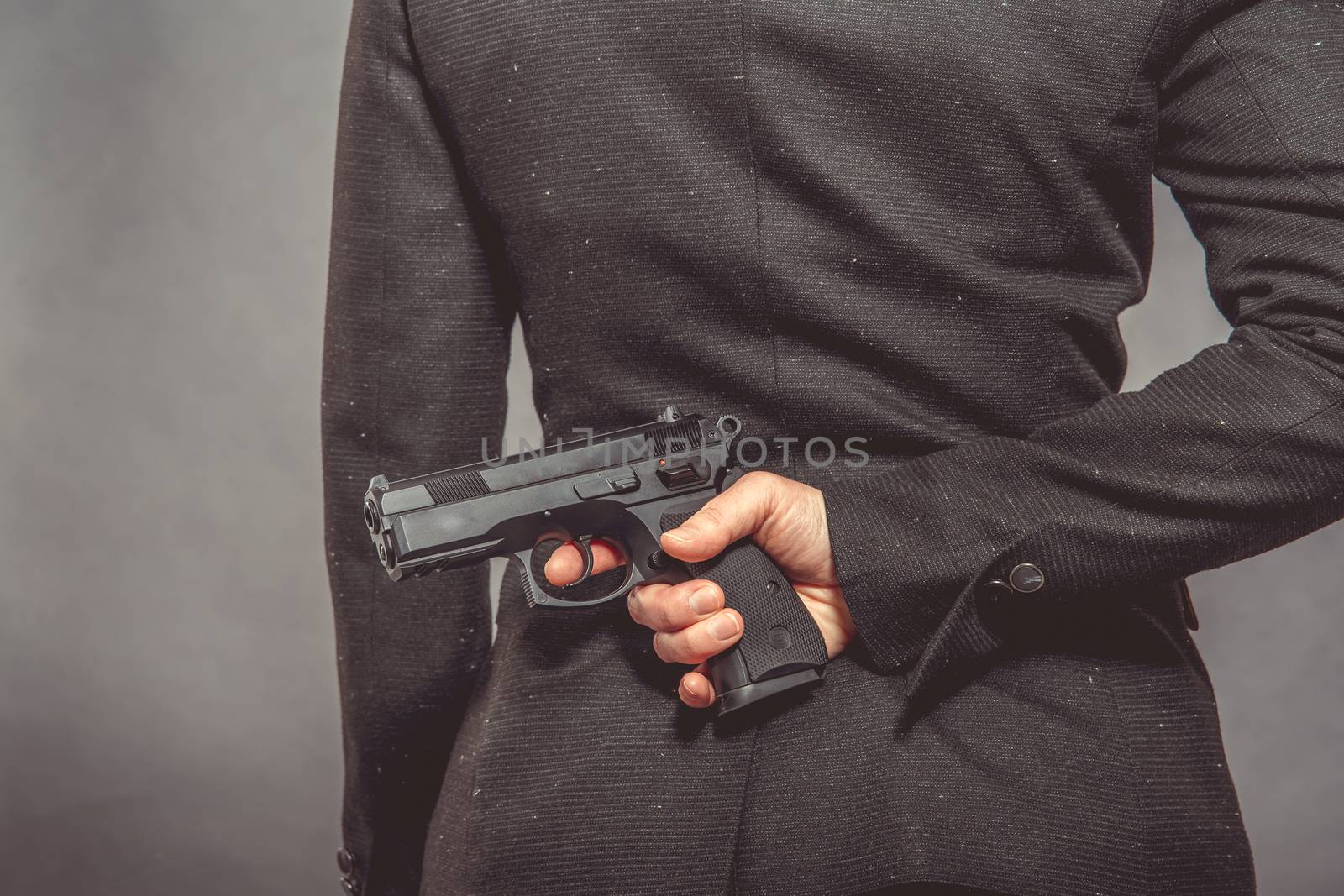 pistol in hand hidden behind agent's back. portrait of woman with gun on grey background, copy space by Edophoto
