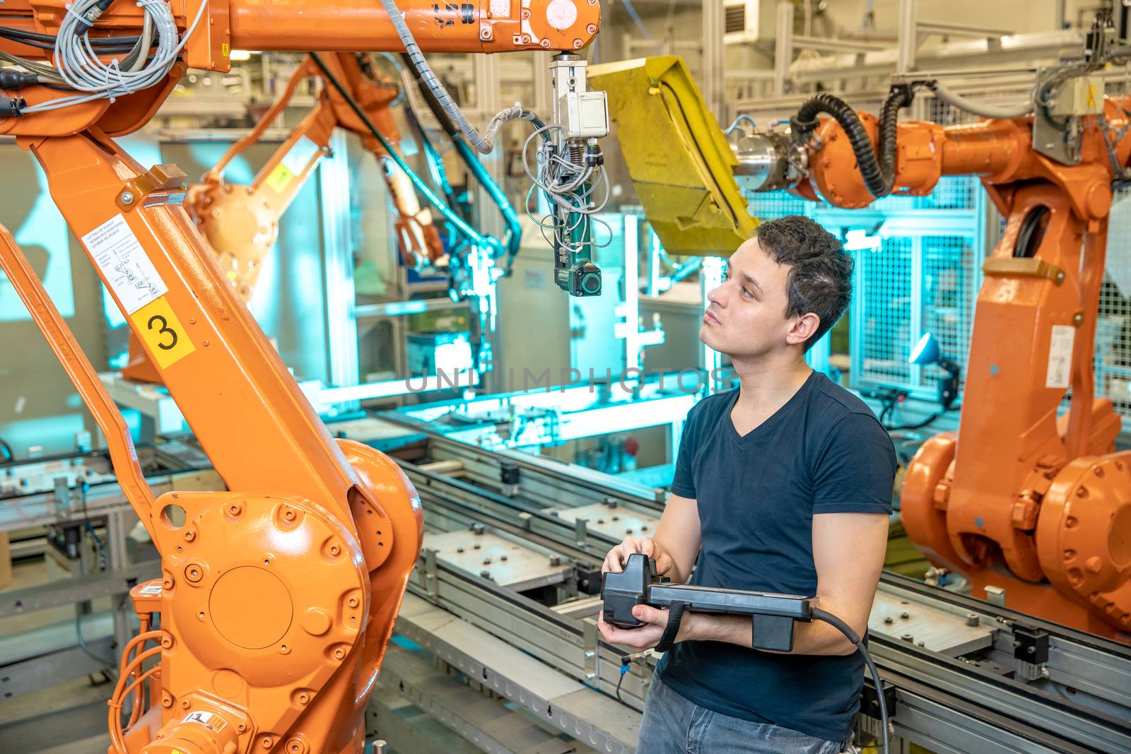 engineer controls using remote control of industrial robot in factory. Automatic welding and gluing using automation and robotic arms by Edophoto