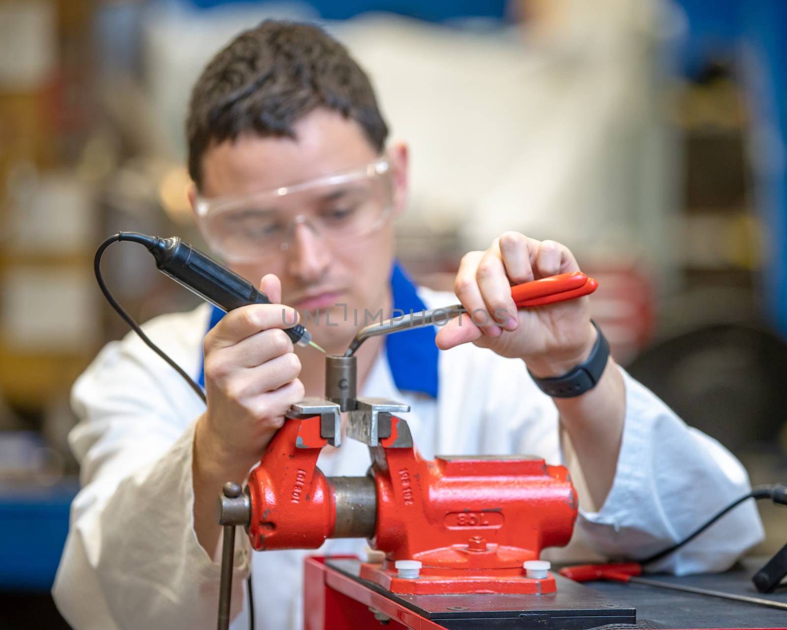 young technician in a factory repairing a machine. man uses a vise to work in the factory.