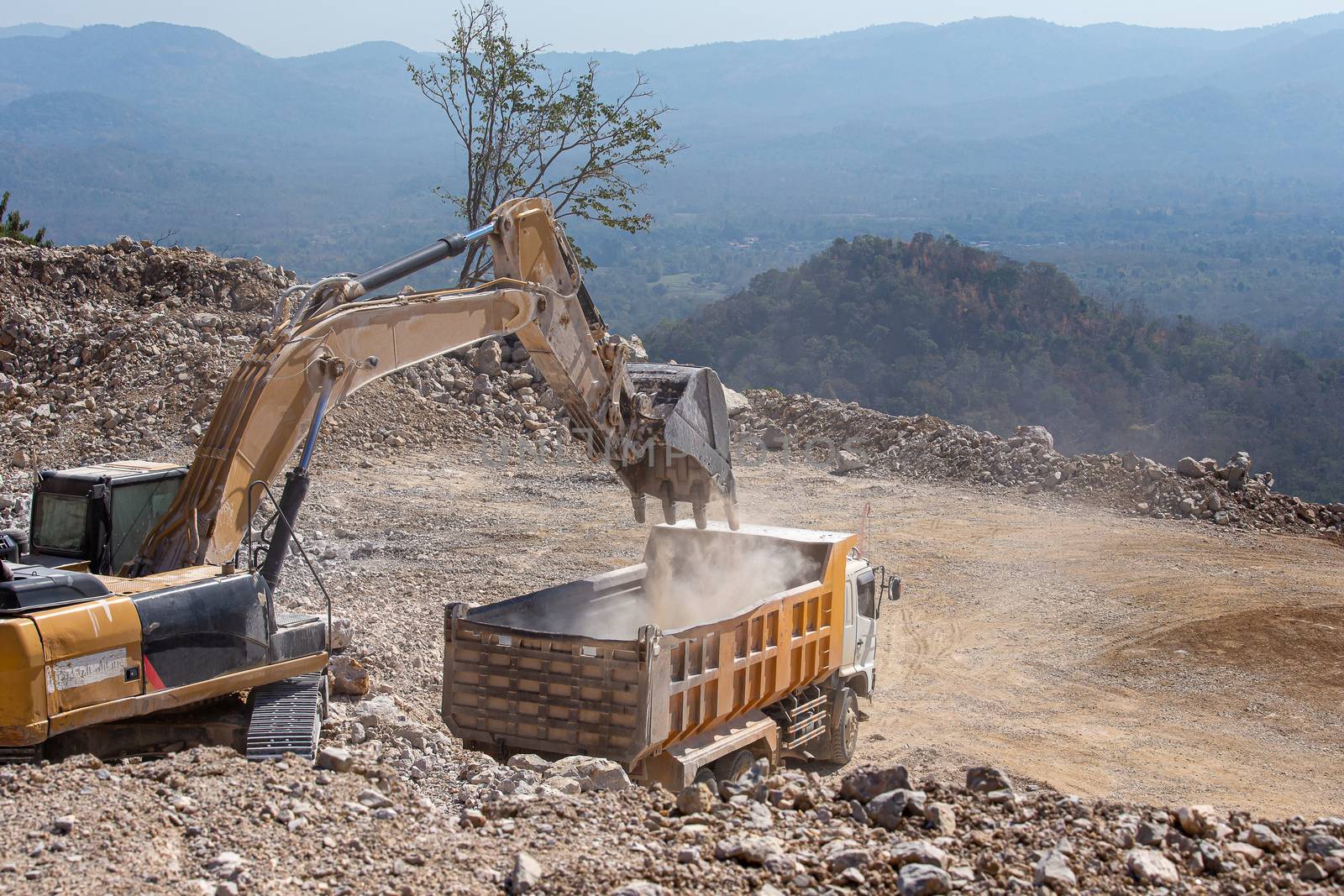 Yellow excavator is filling a dump truck with rocks at coal mine by kaiskynet