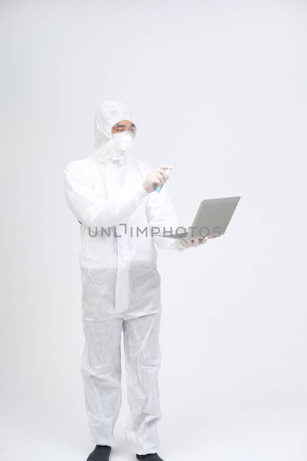 man scientist wearing biological protective uniform suit clothing, mask, gloves spraying sanitizer on computer for sanitizing virus bacteria