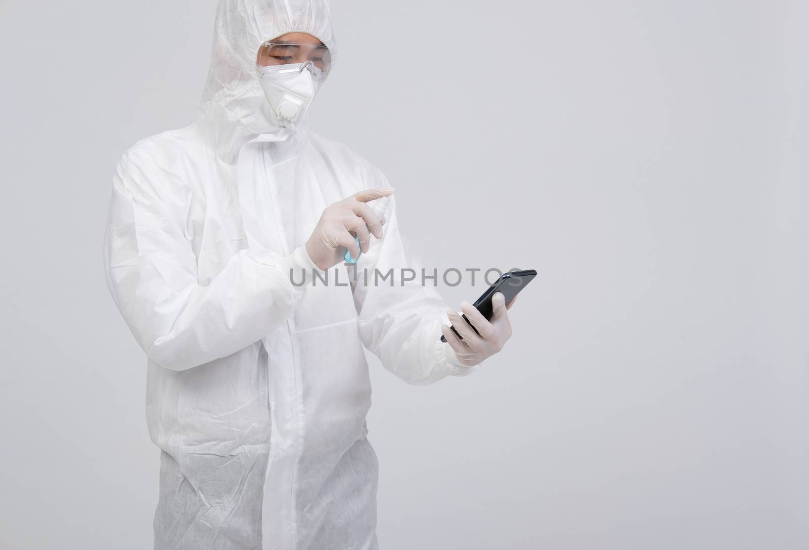 man scientist wearing biological protective uniform suit clothing, mask, gloves spraying sanitizer on smartphone for sanitizing virus bacteria