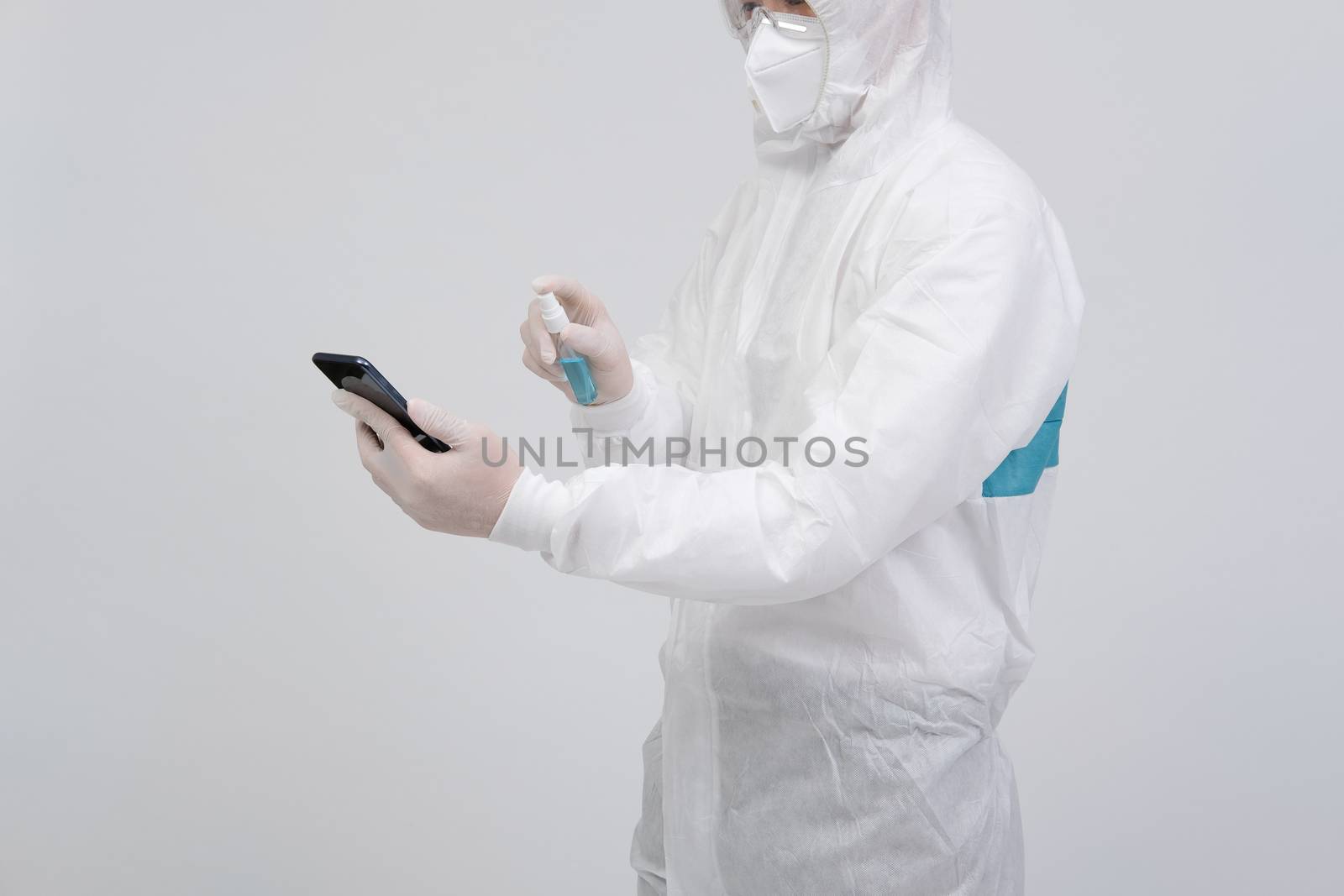 man scientist wearing biological protective uniform suit clothing, mask, gloves spraying sanitizer on smartphone for sanitizing virus bacteria