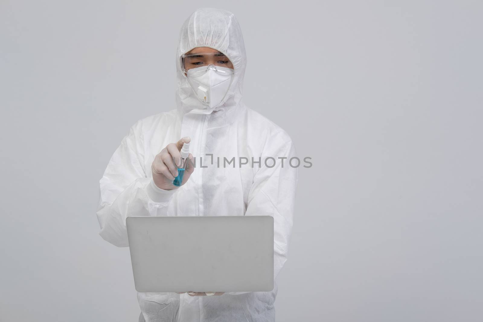 man scientist wearing biological protective uniform suit clothing, mask, gloves spraying sanitizer on computer for sanitizing virus bacteria
