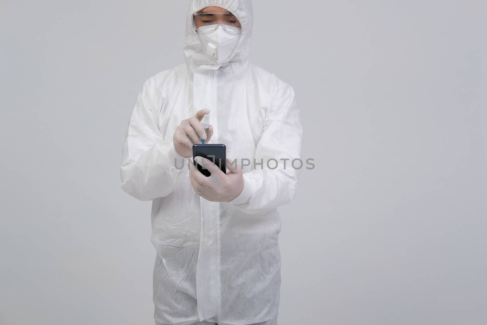 man scientist wearing biological protective uniform suit clothing, mask, gloves spraying sanitizer on smartphone for sanitizing virus bacteria