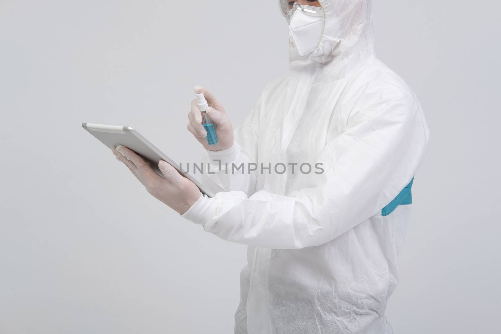 man scientist wearing biological protective uniform suit clothing, mask, gloves spraying sanitizer on tablet for sanitizing virus bacteria
