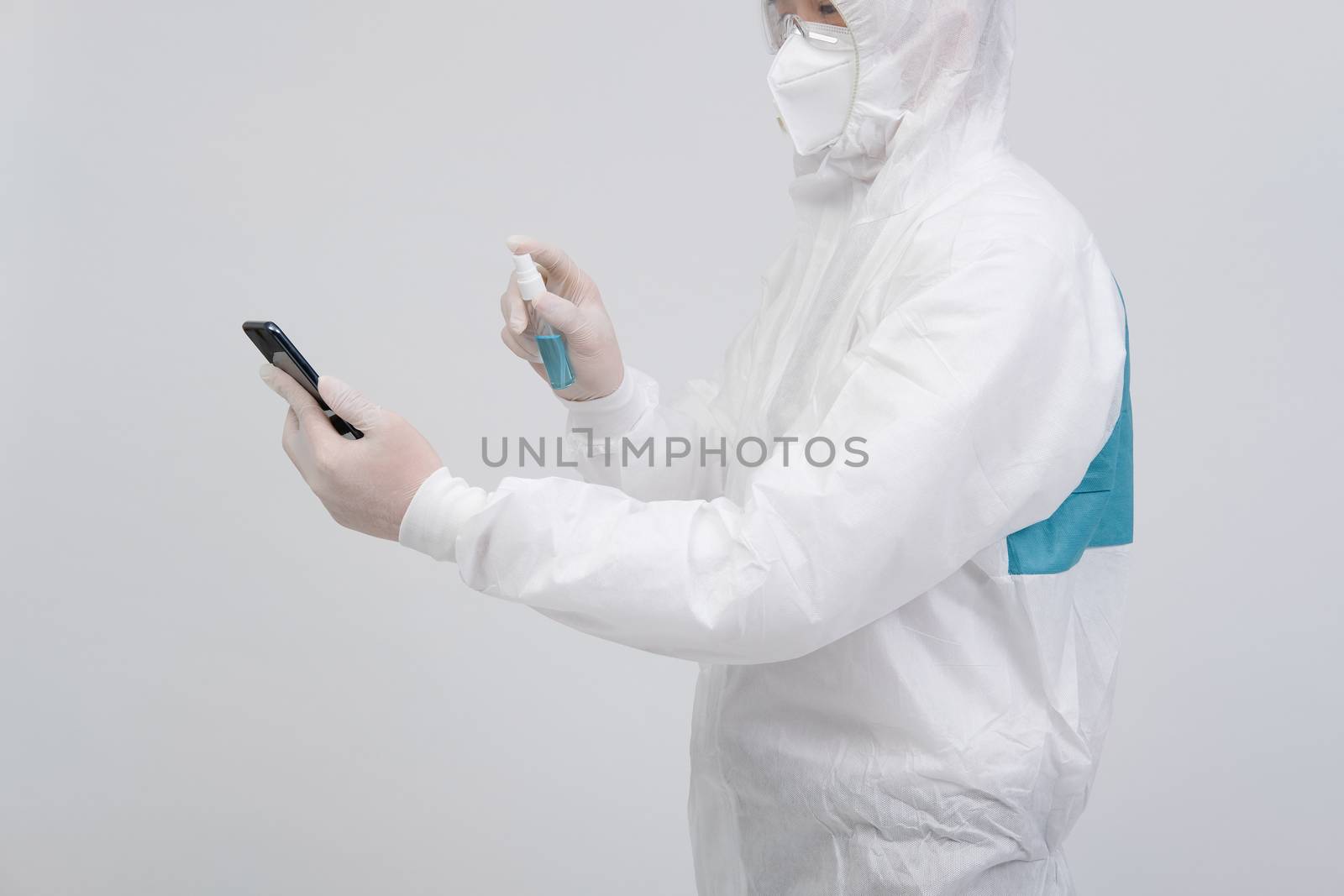 man scientist wearing biological protective uniform suit clothing, mask, gloves spraying sanitizer on smartphone for sanitizing virus bacteria