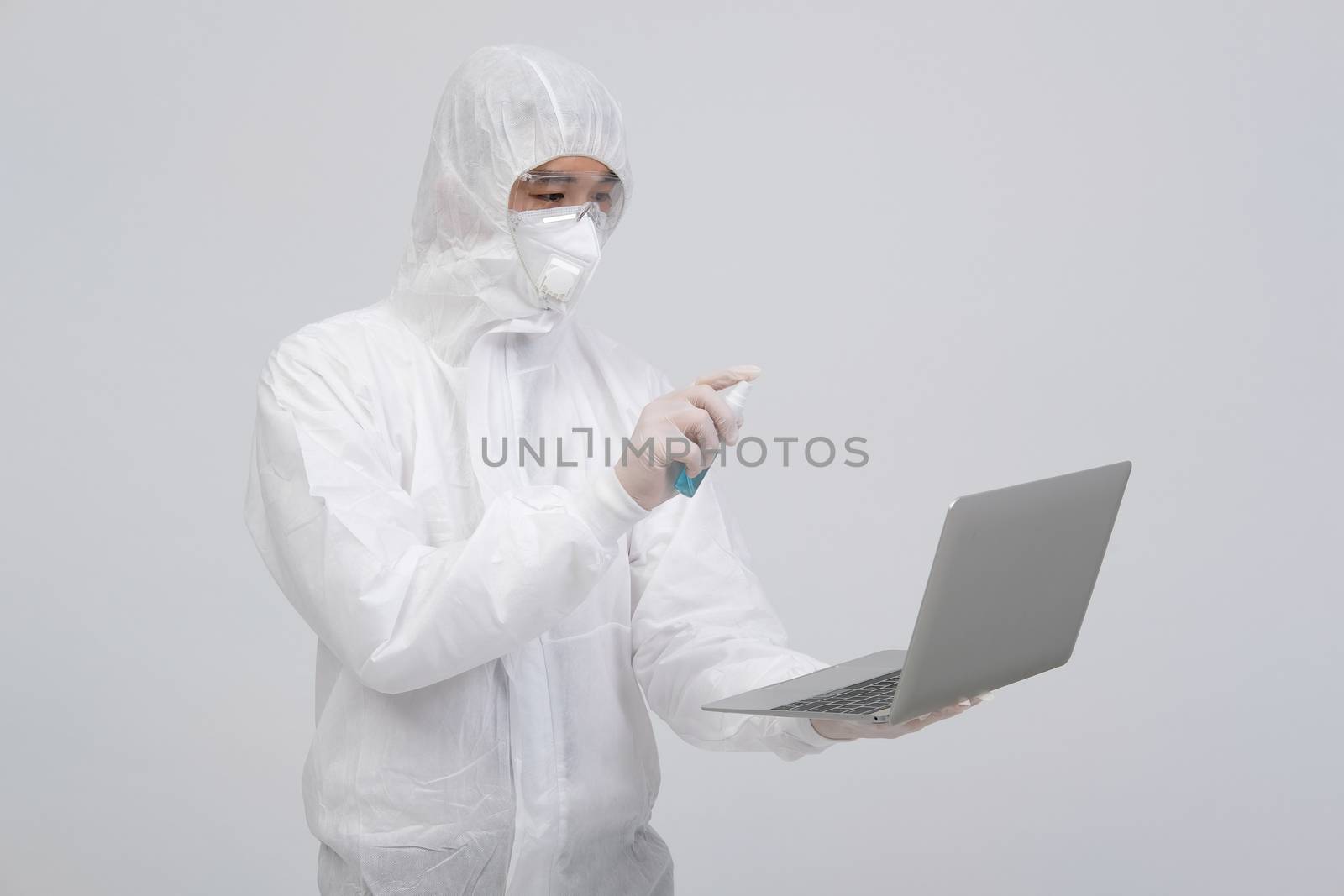 man scientist wearing biological protective uniform suit clothing, mask, gloves spraying sanitizer on computer for sanitizing virus bacteria