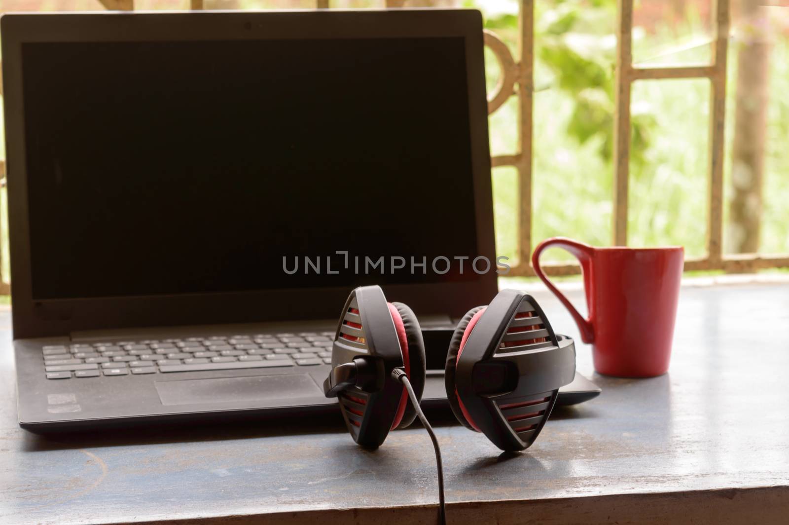 Portable over-ear Binaural Sound USB Headset with Microphone Noise Cancelling and Ultrasonic Volume Adjuster Headphone for Computer, Skype placed near laptop on window sunlight in morning. Red Cup of Coffee at a distance. Stay home, Work from home, Remote Work, Business Continuity background.