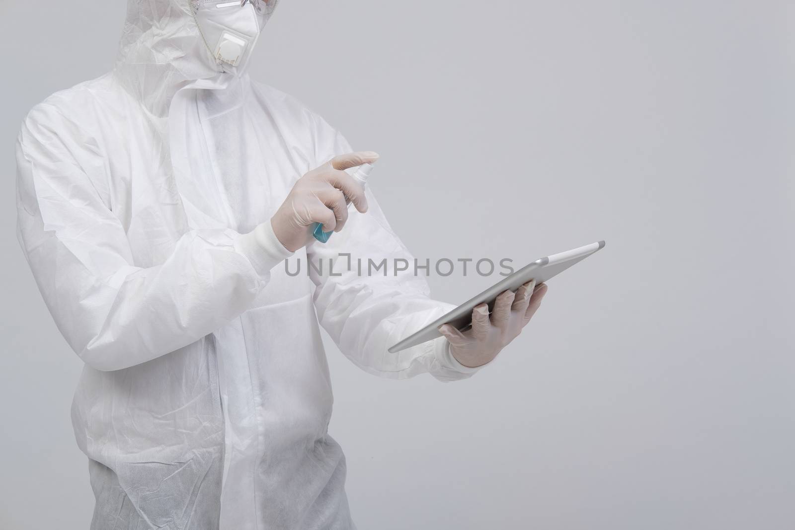 man scientist wearing biological protective uniform suit clothing, mask, gloves spraying sanitizer on tablet for sanitizing virus bacteria