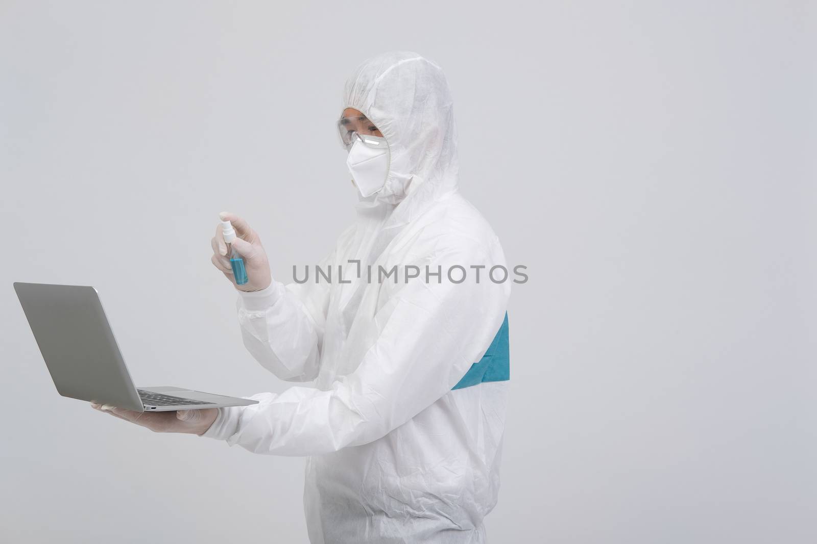 man scientist wearing biological protective uniform suit clothing, mask, gloves spraying sanitizer on computer for sanitizing virus bacteria