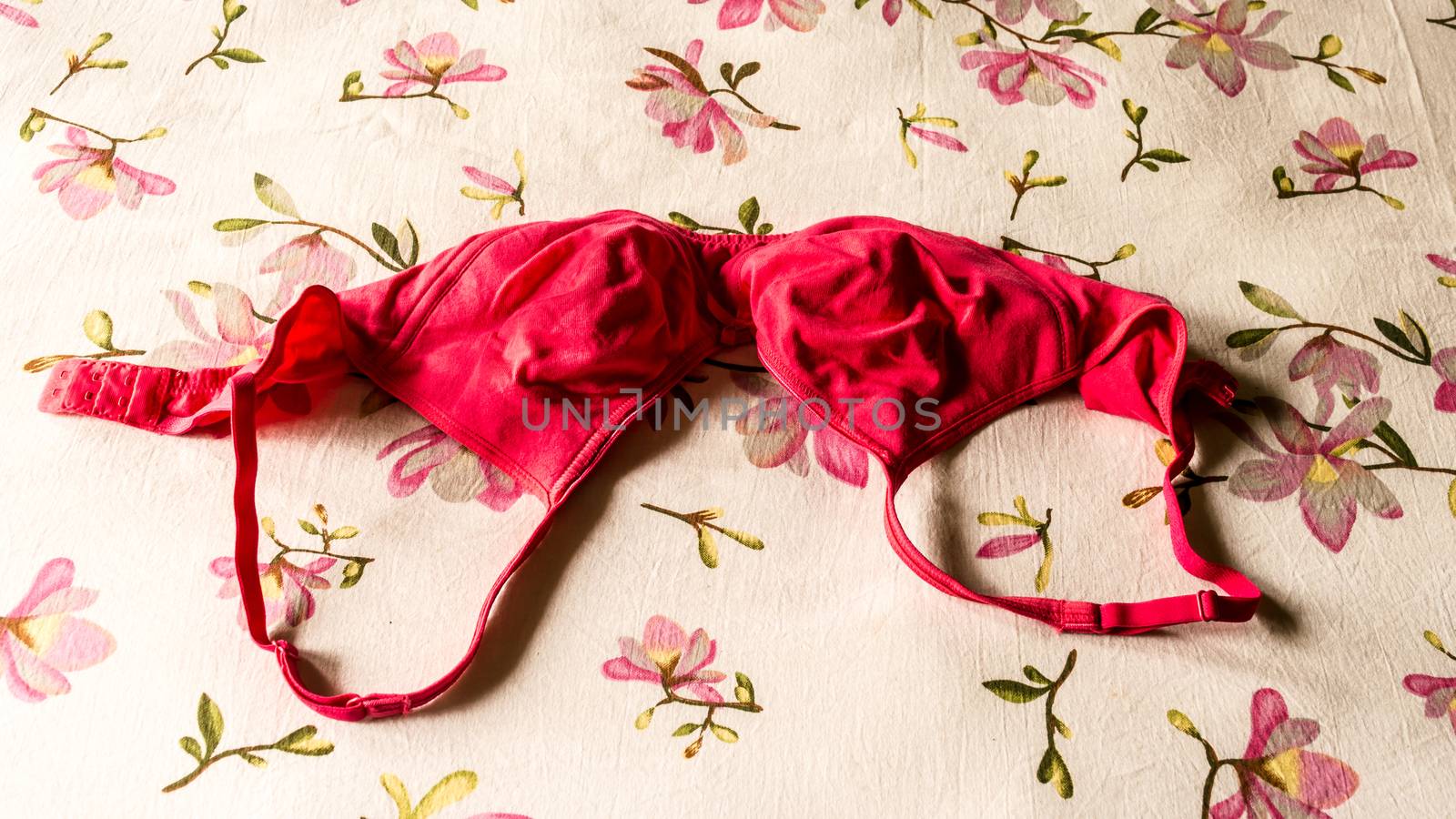 Red bra on morning bed sheet. Sunlight from window. Romantic passion female lingerie. Sexy fashion background. Still life.