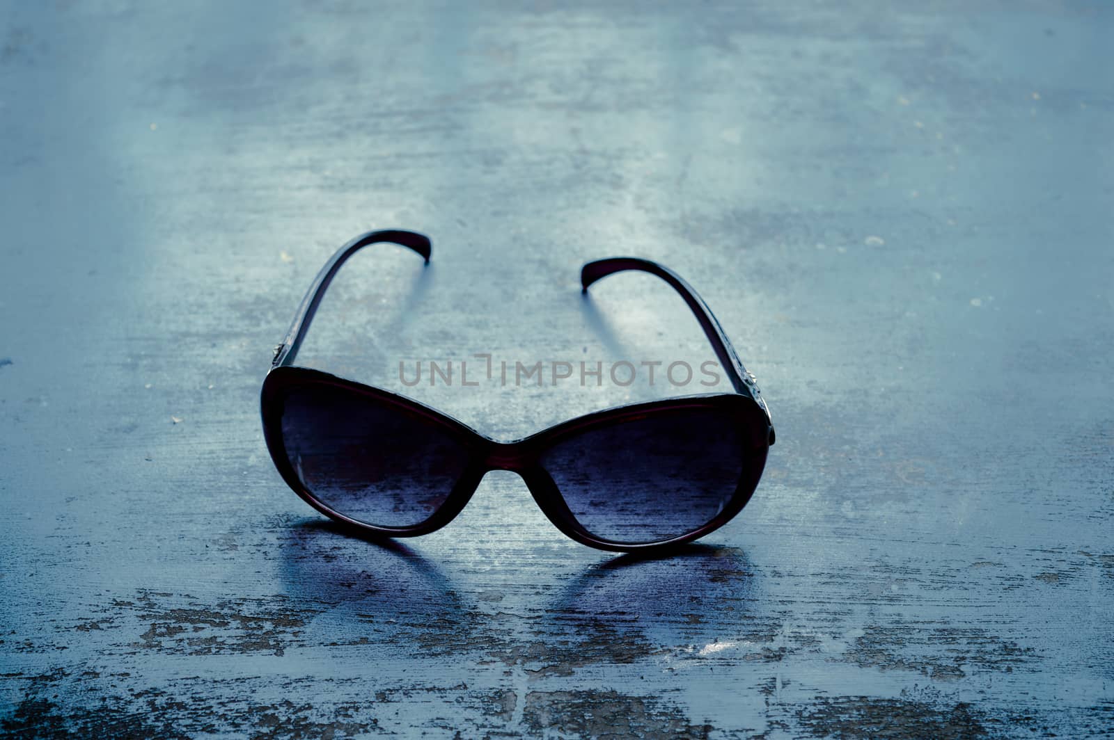 Blue modern fashionable Sunglasses on rustic floor. Fashion background. Still life photography. Sunlight reflection from back. Lens shadow on floor.