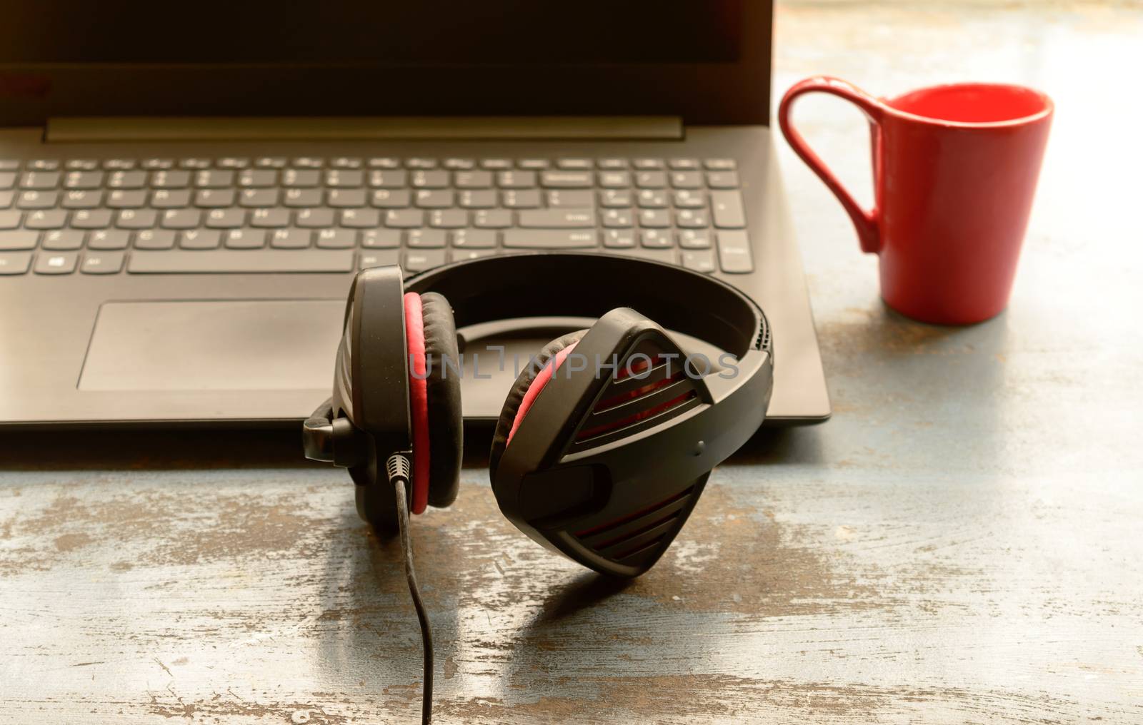 Portable over-ear Binaural Sound USB Headset with Microphone Noise Cancelling and Ultrasonic Volume Adjuster Headphone for Computer, Skype placed near laptop on window sunlight in morning. Red Cup of Coffee at a distance. Stay home, Work from home, Remote Work, Business Continuity background.