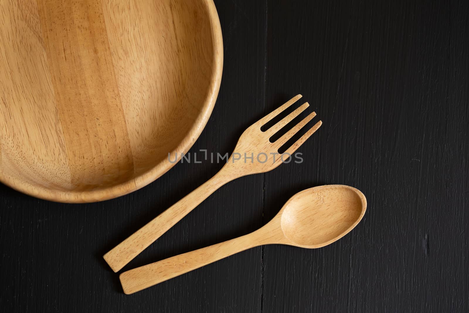 Spoons, forks and Dish made of wood on the black wooden background.