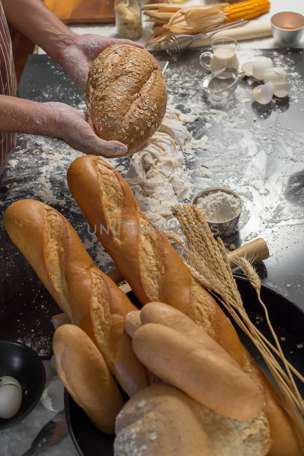 Chef holds the fresh bread in hand. Man preparing buns at table in kitchen.
