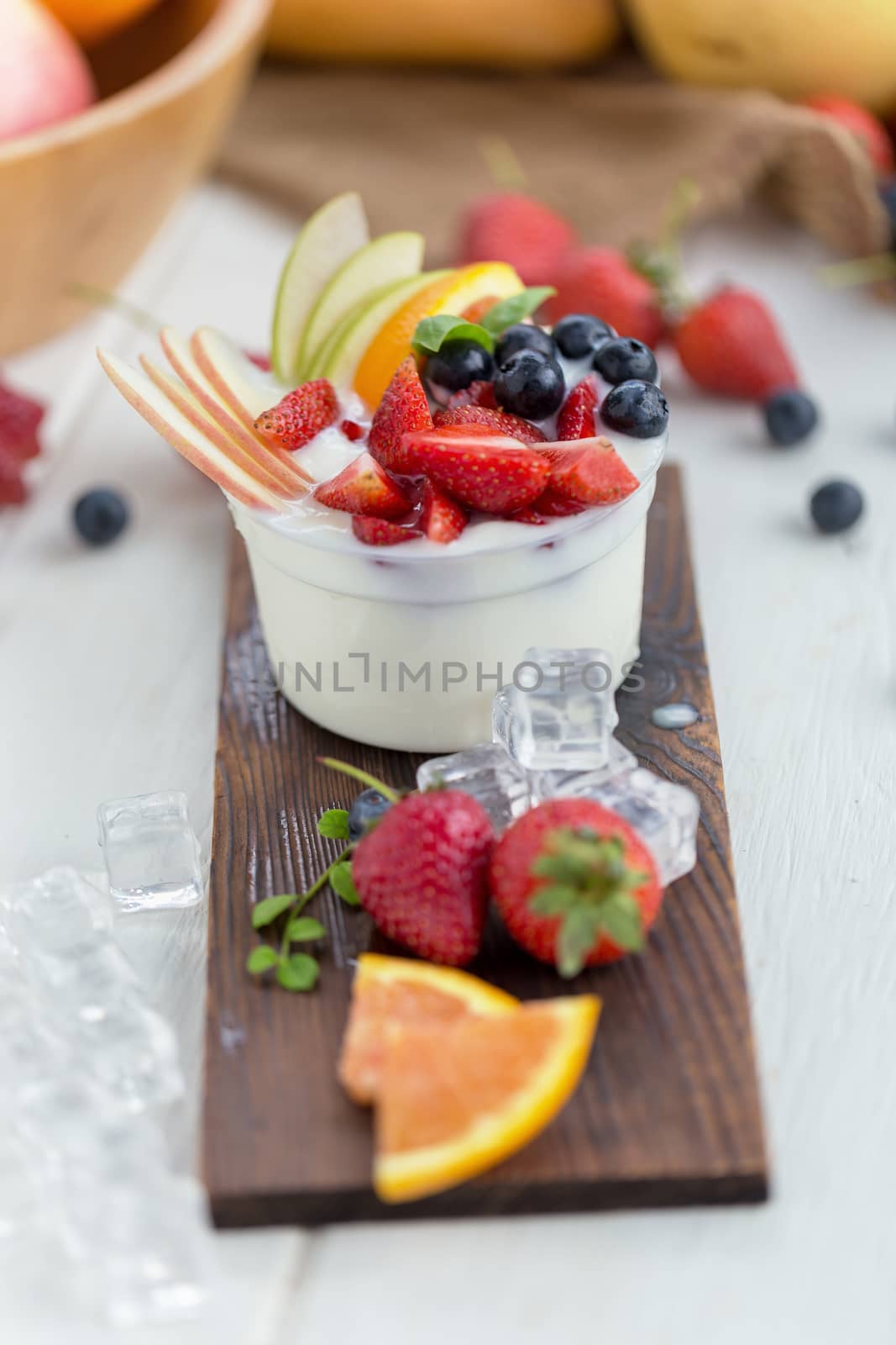 Healthy fruit salad with yoghurt on a wooden plate with ice cube by kaiskynet