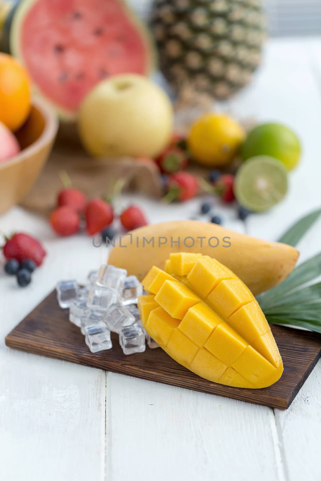 Ripe Mango on a wooden plate with ice cubes and fruit as background.