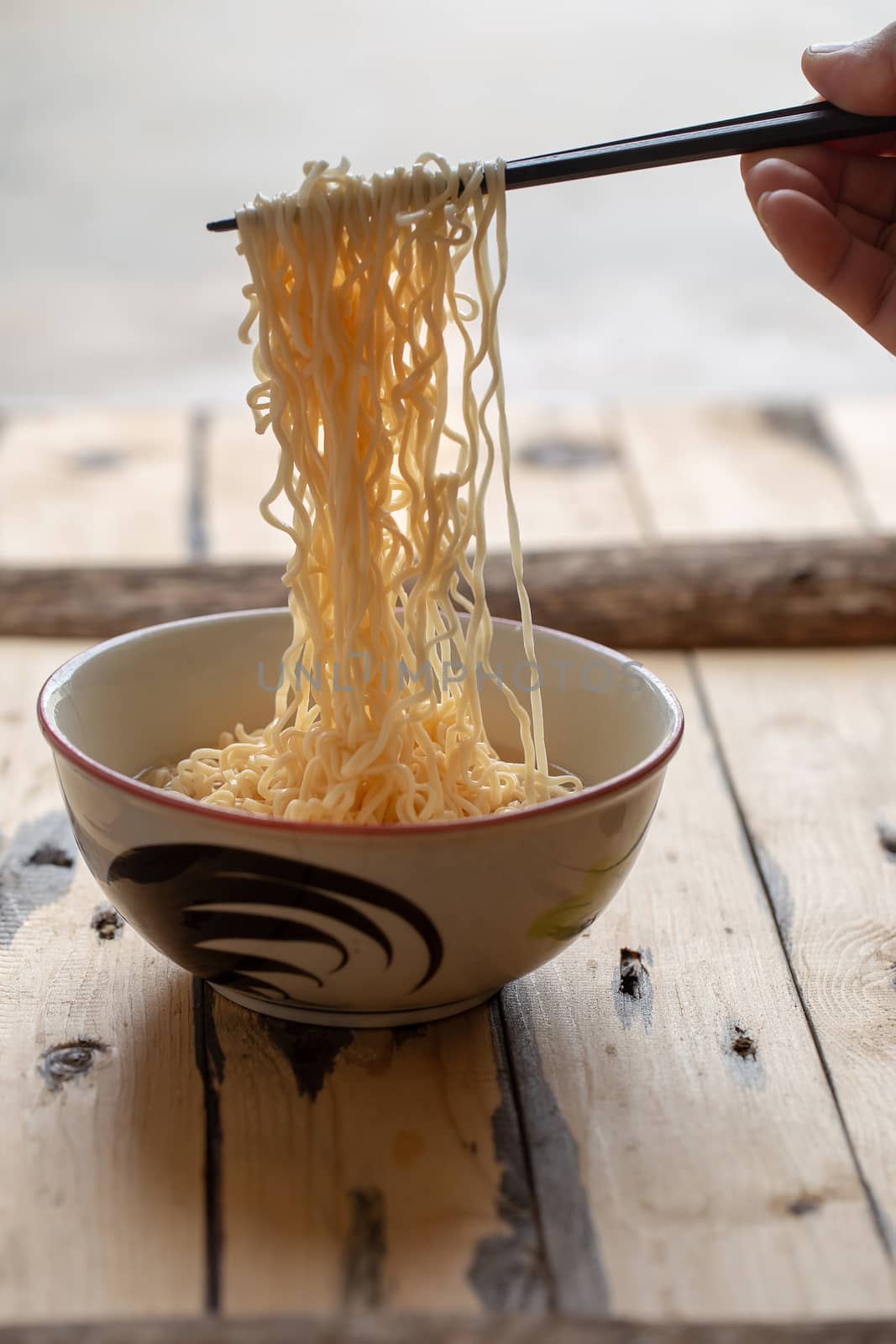 Hand uses chopsticks to pickup tasty noodles in bowl on wooden b by kaiskynet