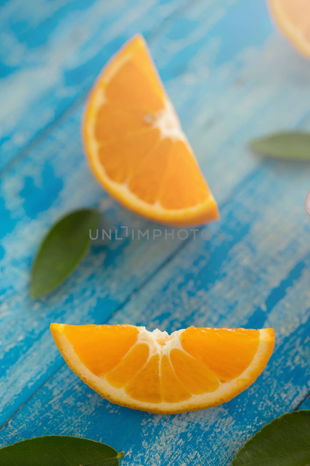 Orange sliced and leaves on blue wooden background by kaiskynet