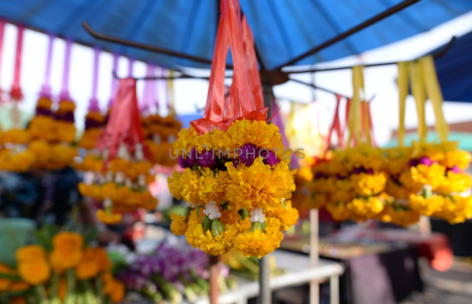 The garland is made of bright yellow flowers. Was hung for sale in the market, blurred background.