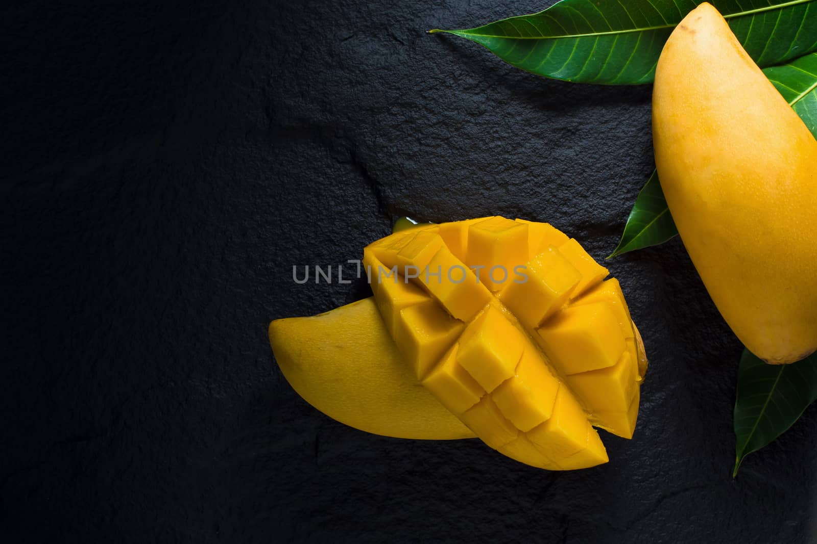 Ripe golden mangos with leaf on dark background.