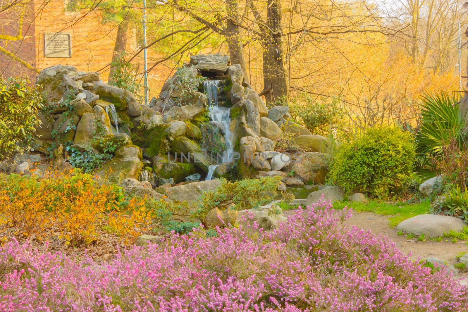 a waterfall descends gently between the rocks in a pond of a flowered  park