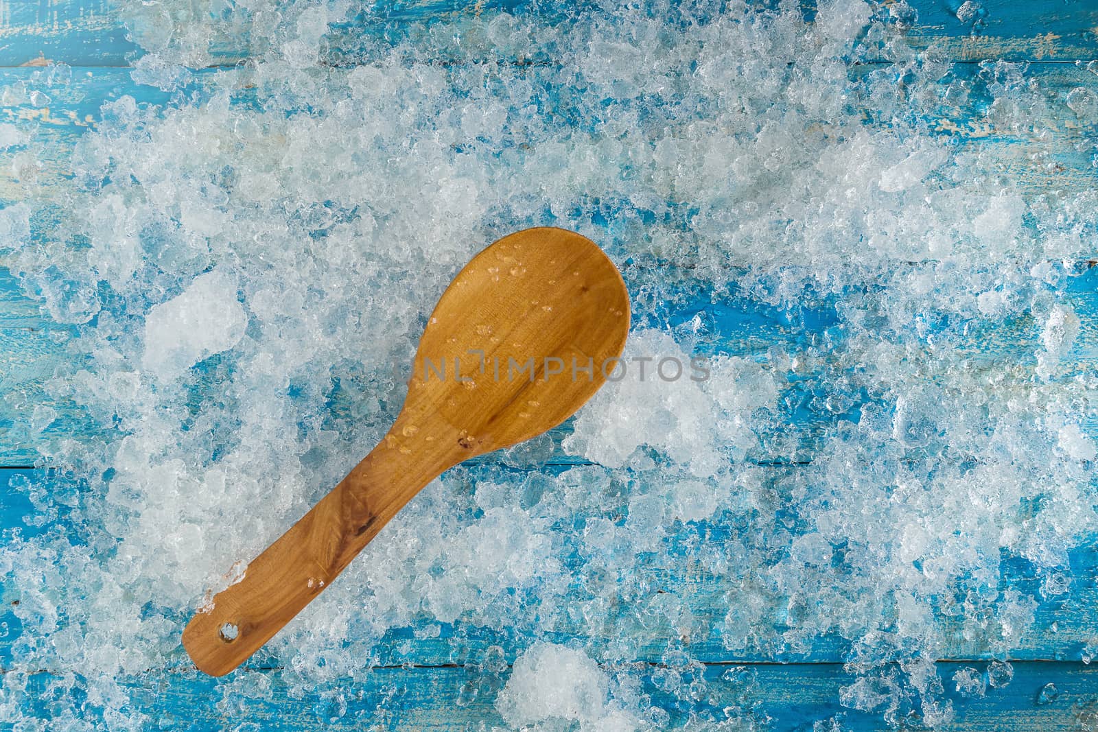 Crushed ice cubes and wooden spoon on vintage blue wooden table. Top view.